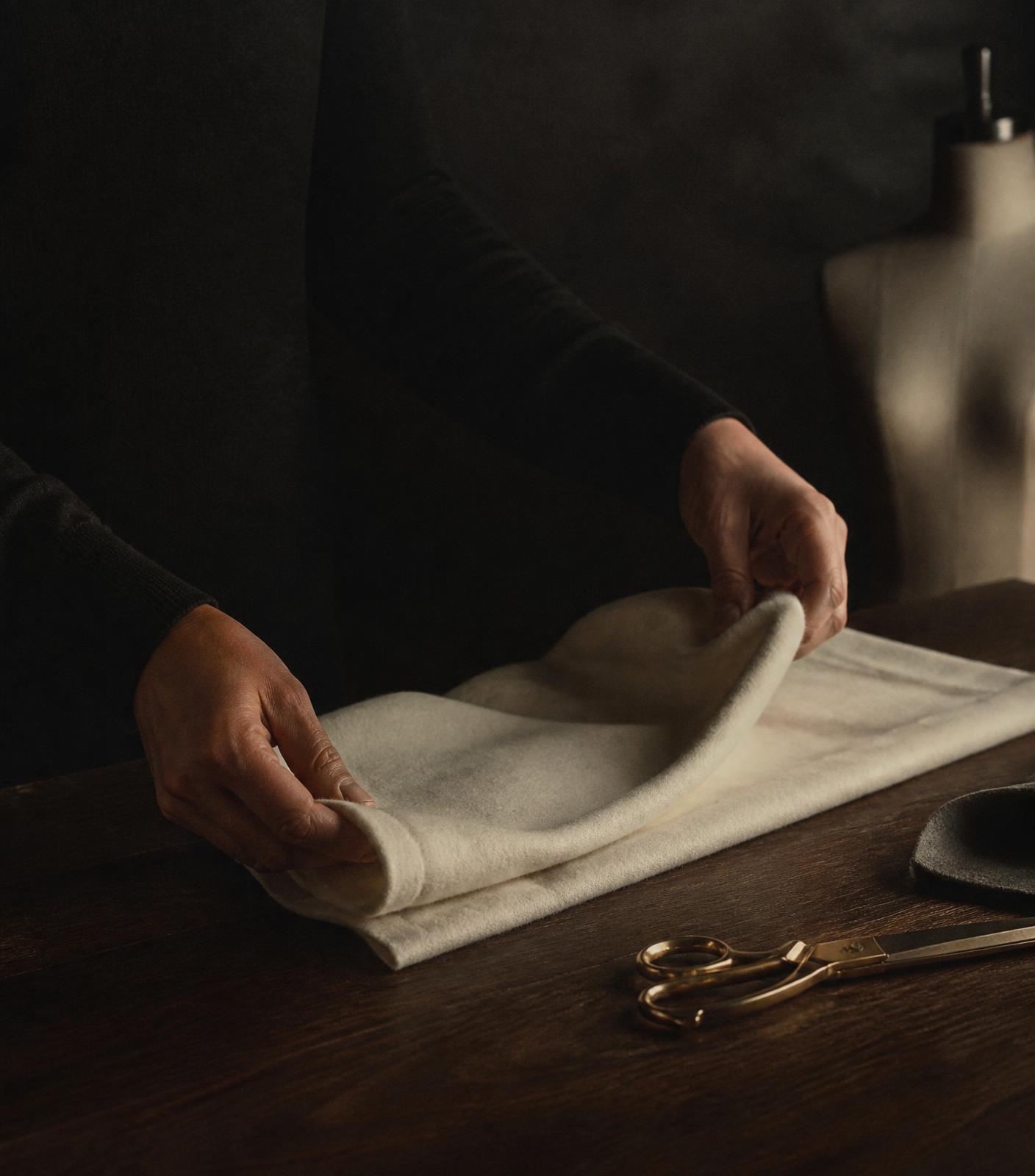 Hands folding ivory cashmere in the VELORA atelier